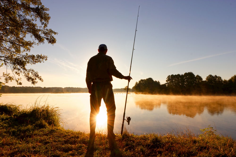 Silhouette of man fishing next to a lake 