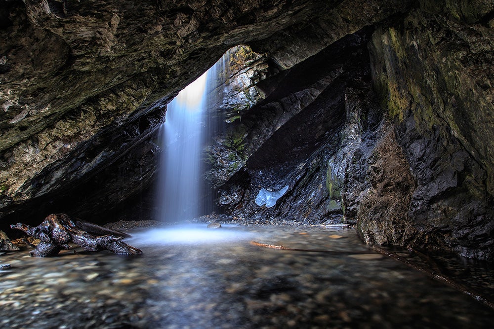 light shining through a hole in the ceiling of a stone cave with water running through it