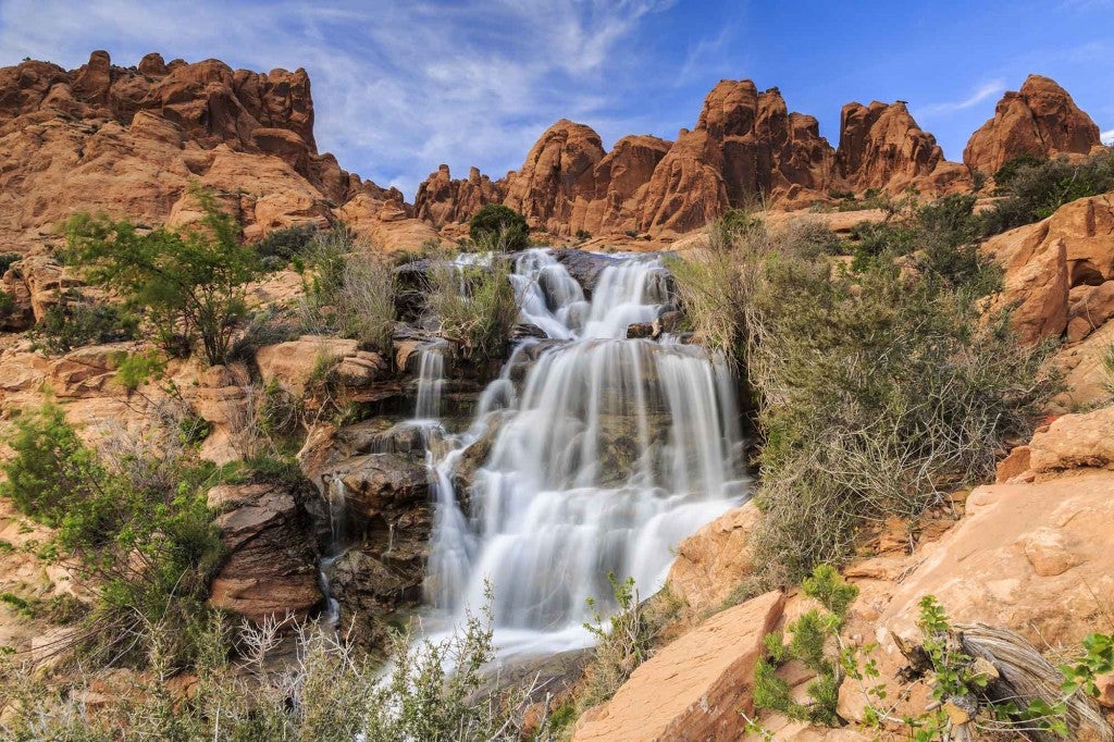 a waterfall careens over red rocks in the desert of utah