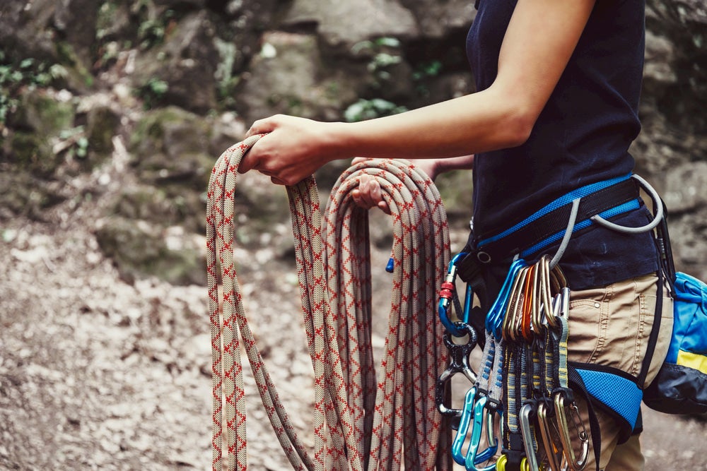 Closeup of female torso wearing climbing harness with equipment attached, and rope in hand.