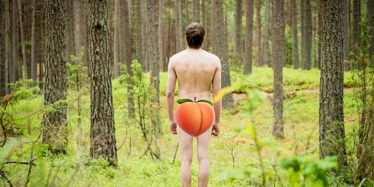 a man stands naked in the woods with a peach emoji over his rear end
