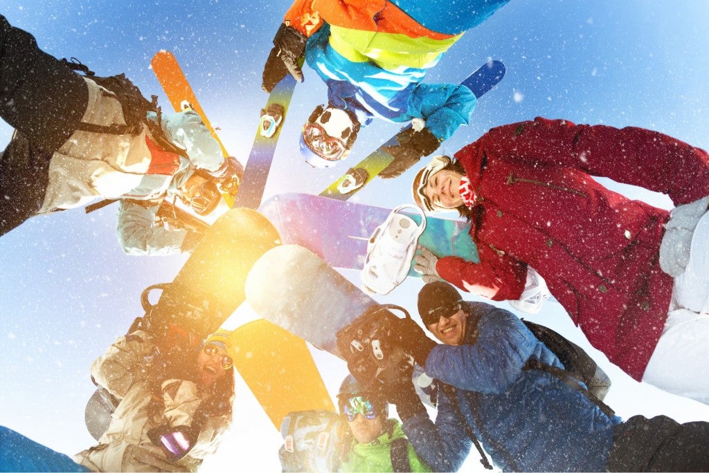 group of skiiers and snowboarders looking down on camera in a jovial circle