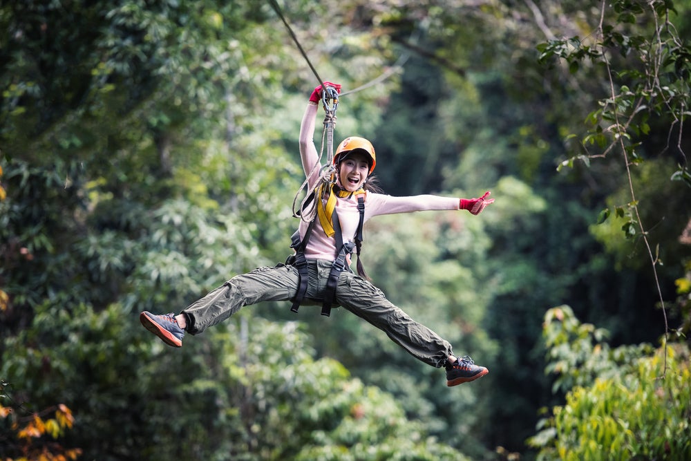 Woman zip lining and smiling with trees surrounding her 