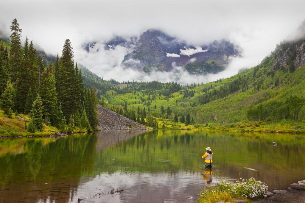Fly fisher wading in a river below the Colorado rockies.