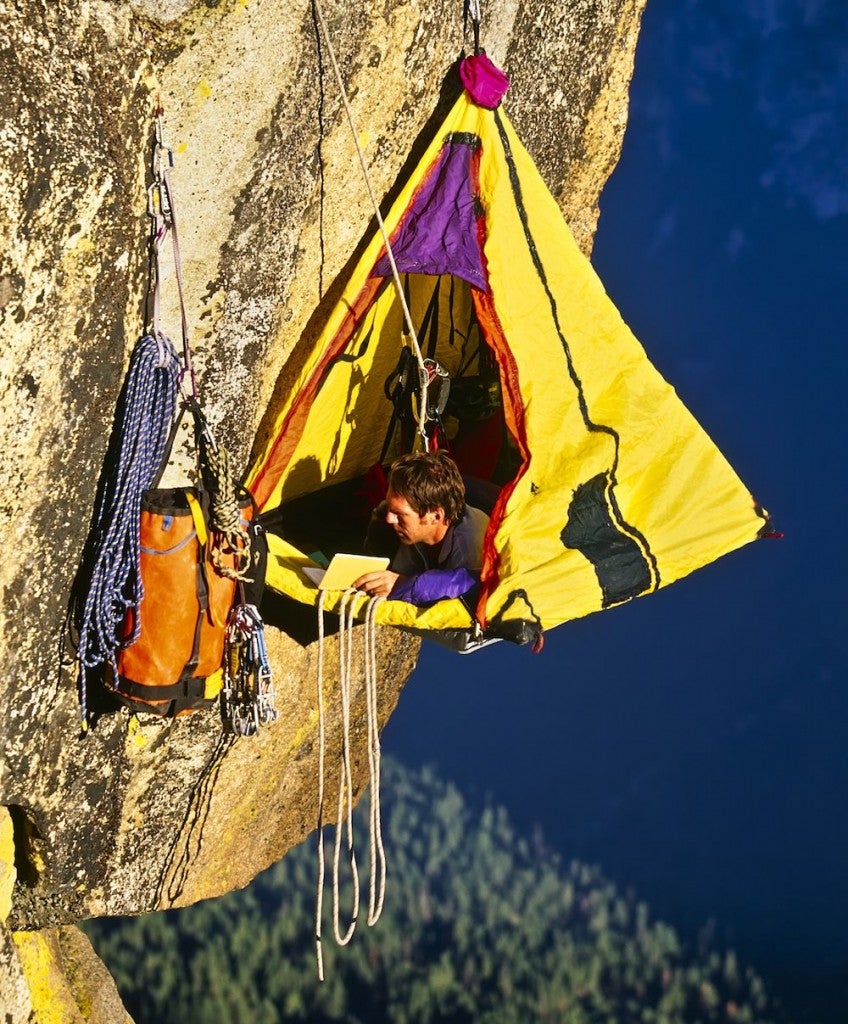 Rock climber bivouacked in his vertical camping portaledge on an overhanging cliff.