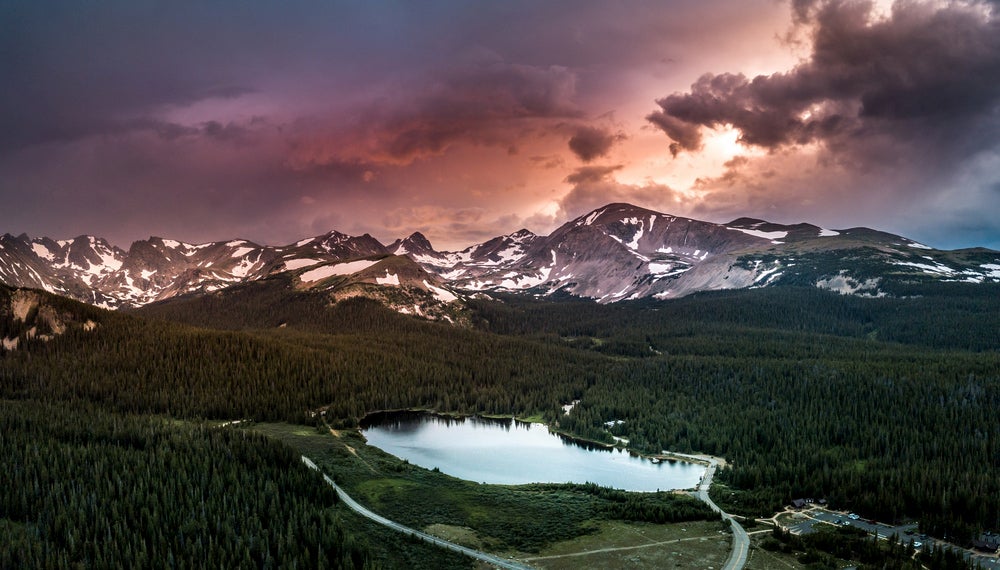 Aerial view of Indian Peaks Wilderness lake and snow capped mountains at sunset.