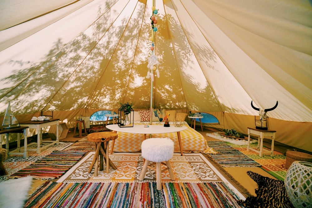 Large tent with colorful carpets and fuzzy chairs with tree silhouette in background 