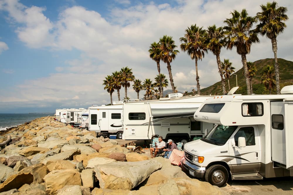 rvs parked along rock wall and beach with palm trees