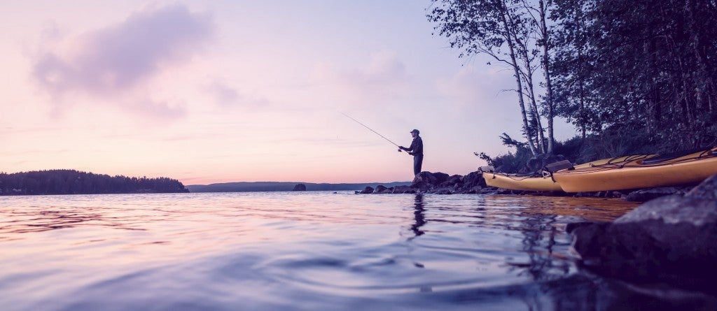 Fisherman at dusk on a lake next to kayaks.