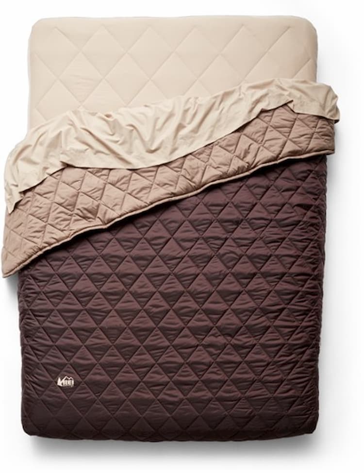 a camping air mattress set up with a quilt and sheet