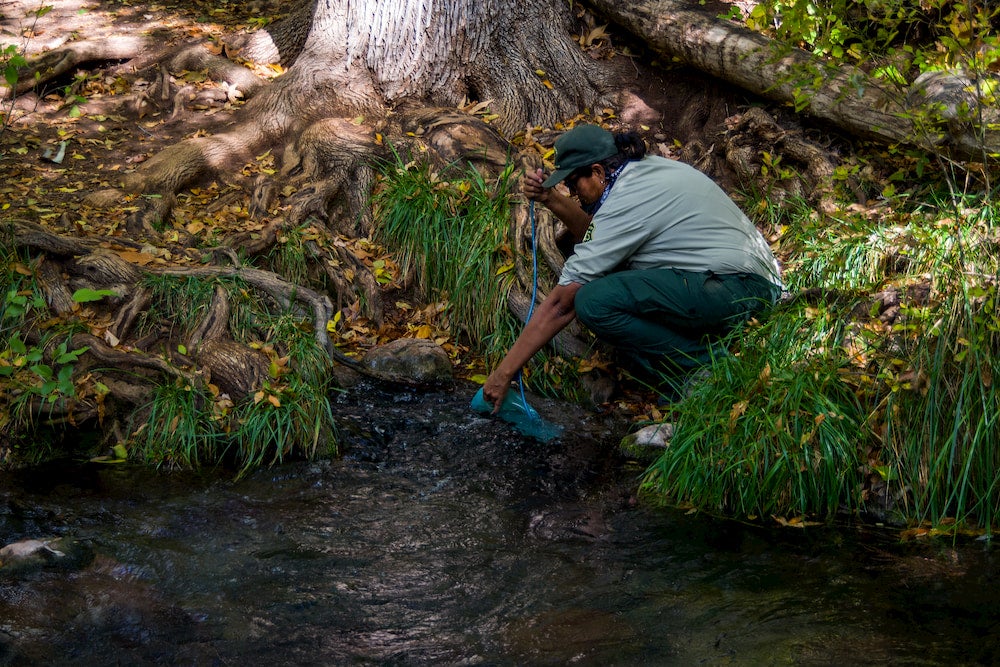 a park ranger fills her water bladder in a river