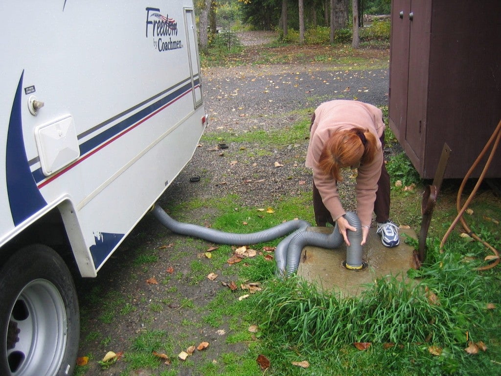 a woman holds a tube to drain a toilet tank in an RV