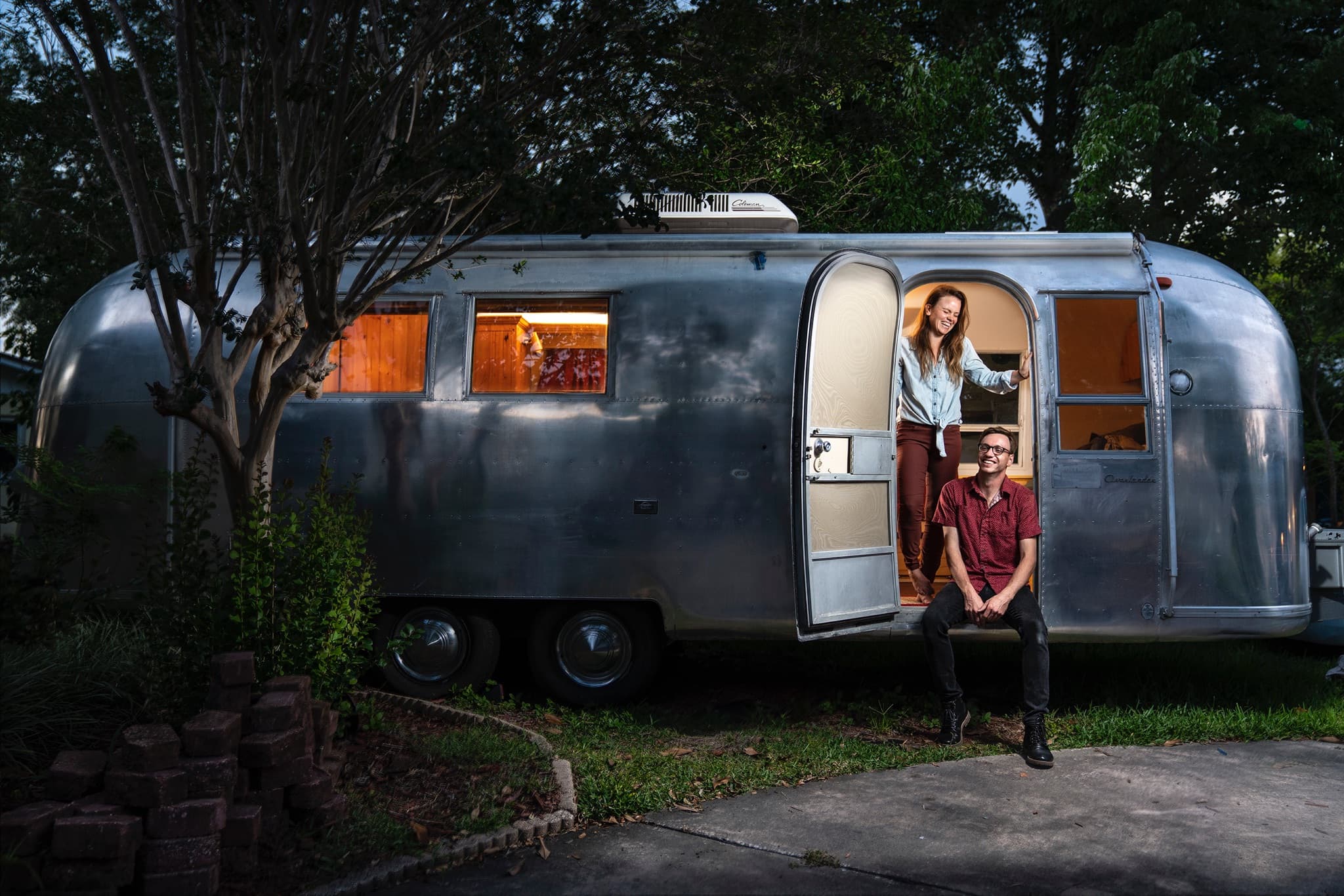 a woman next to a man at the entrance to an airstream trailer parked at a campground