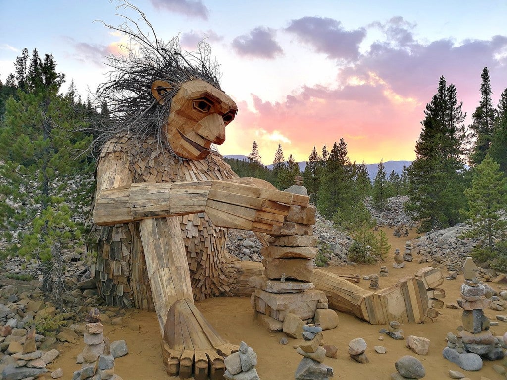 Isak Heartstone the wooden troll sculpture sitting on the ground building a rock carin