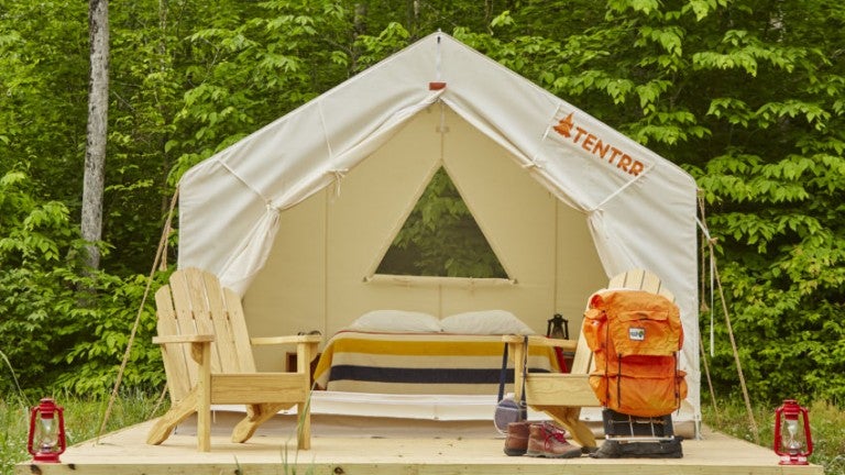 a tentrr glamping tent in maine set up with chairs, a bed and a tent on wood