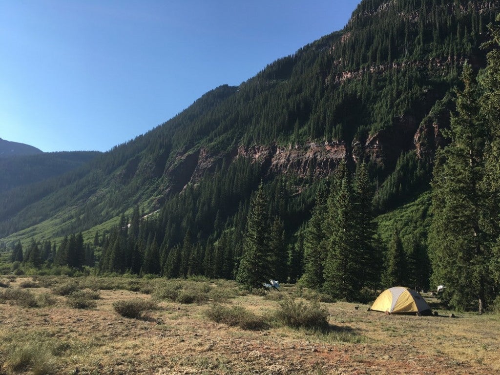 a yellow tent at the edge of a tree covered mountain