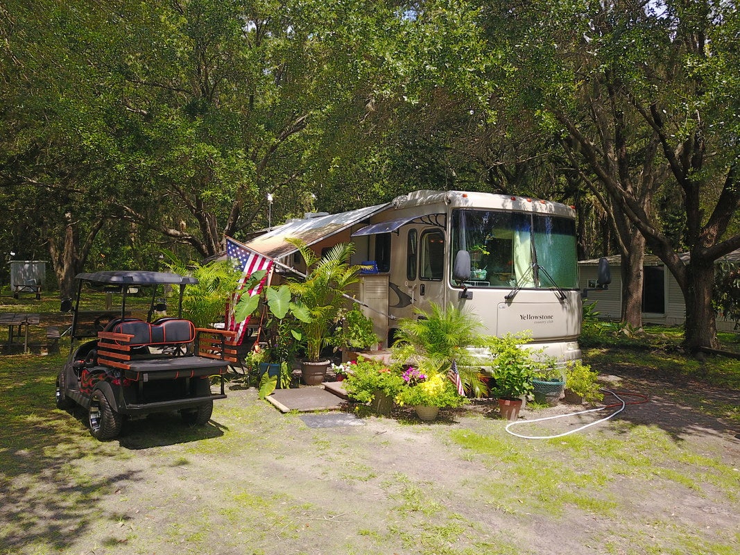 a stationed RV surrounded by flowers and trees on a grass campground next to a golf cart