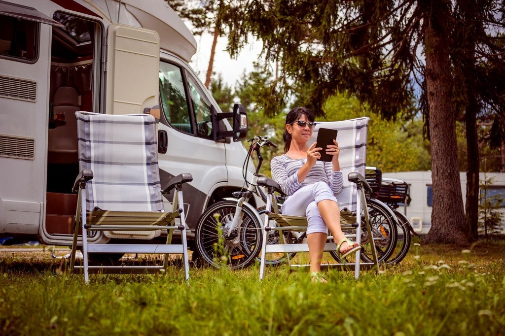 a woman holding a phone in a camping chair near an RV at a campground