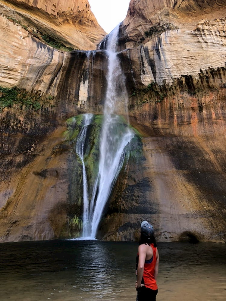a woman stares at the bottom of a waterfall in utah