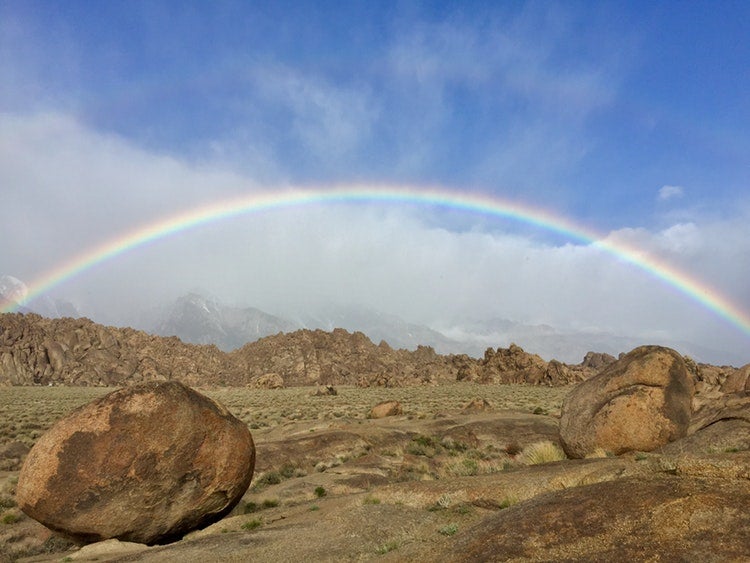 a rainbow stretches over rock carins in a desert in california