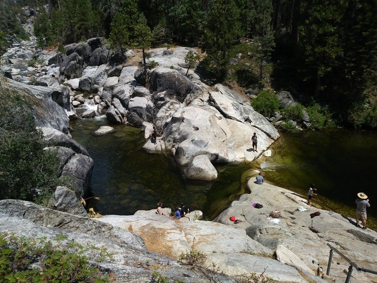 visitors play in small pools of water surrounded by smooth rocks on a river in california