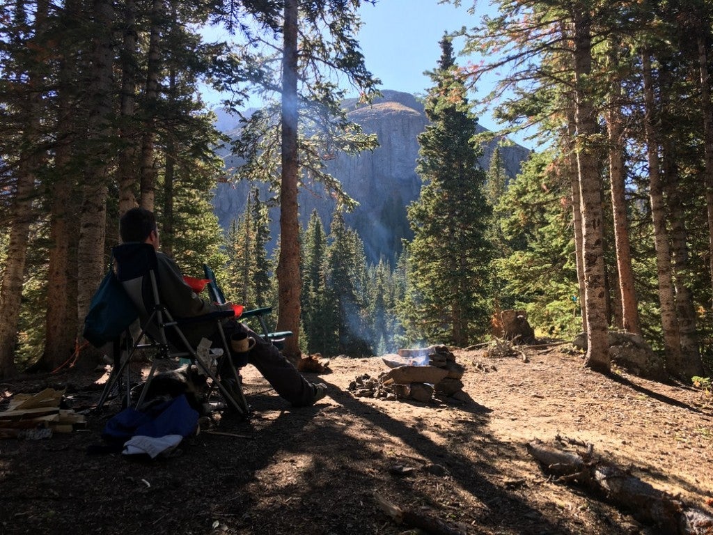 a man in a camping chair next to a fire overlooking a cliff while camping