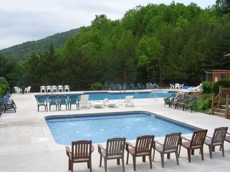a row of pool chairs in front of two pools near a line of trees