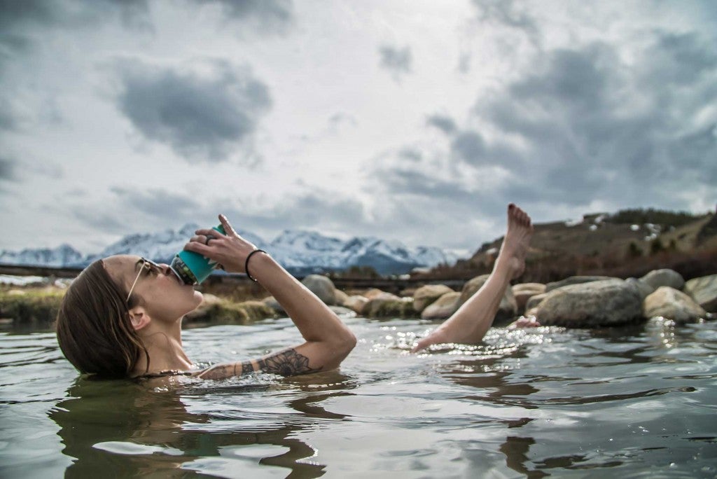 a woman bathes in one of many idaho hot springs while drinking from a can