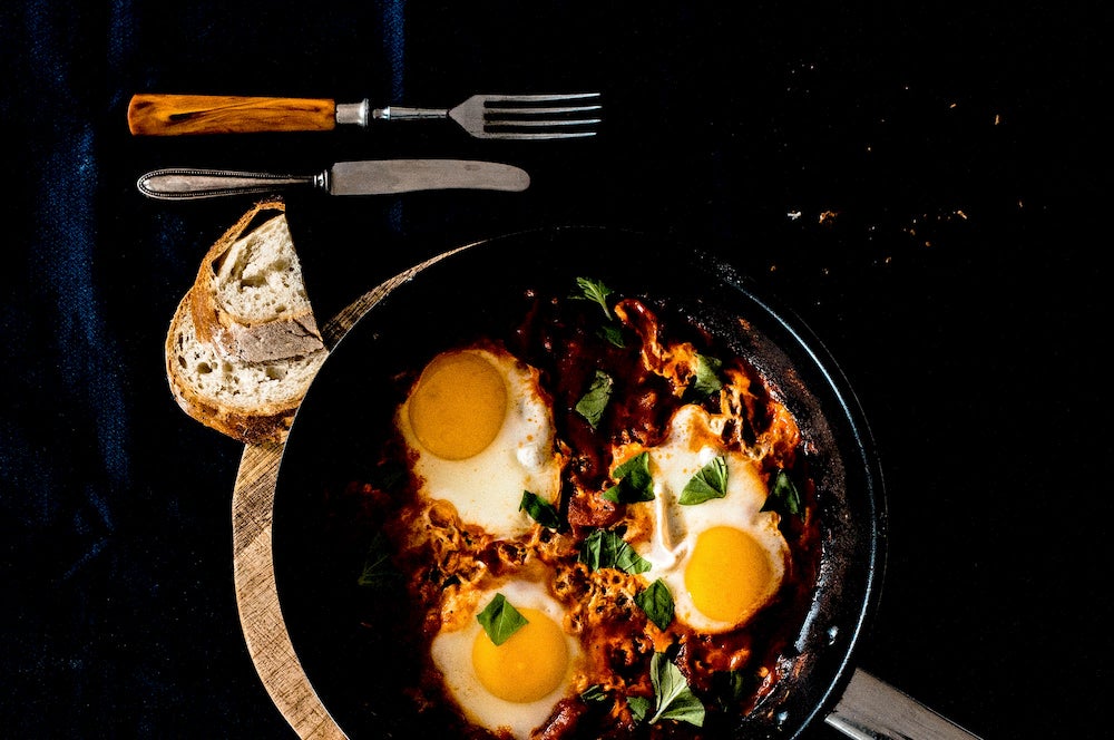 Silverware and bread surround a cast iron skillet full of eggs 