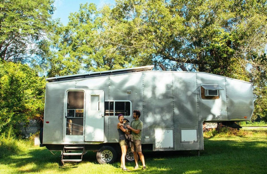 two people and a dog in front of an RV at a campground