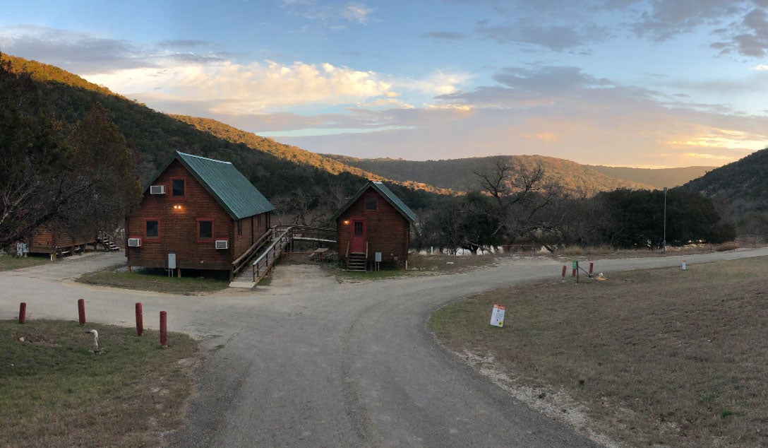 two wooden cabins nestled in between grassy hills in texas