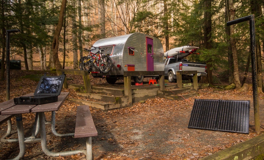 a campsite with a car and campervan, a portable charger on a picnic table and a solar camping generator 