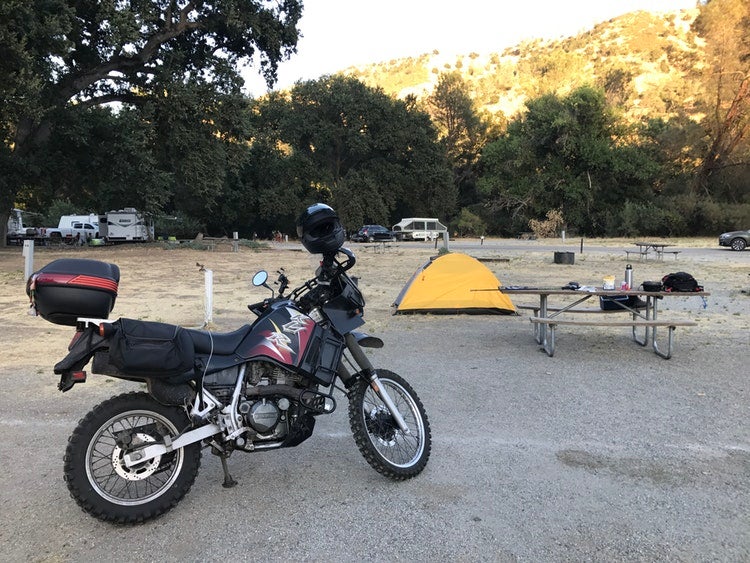 una moto, una tienda de campaña y una mesa de picnic descansando en un camping de california
