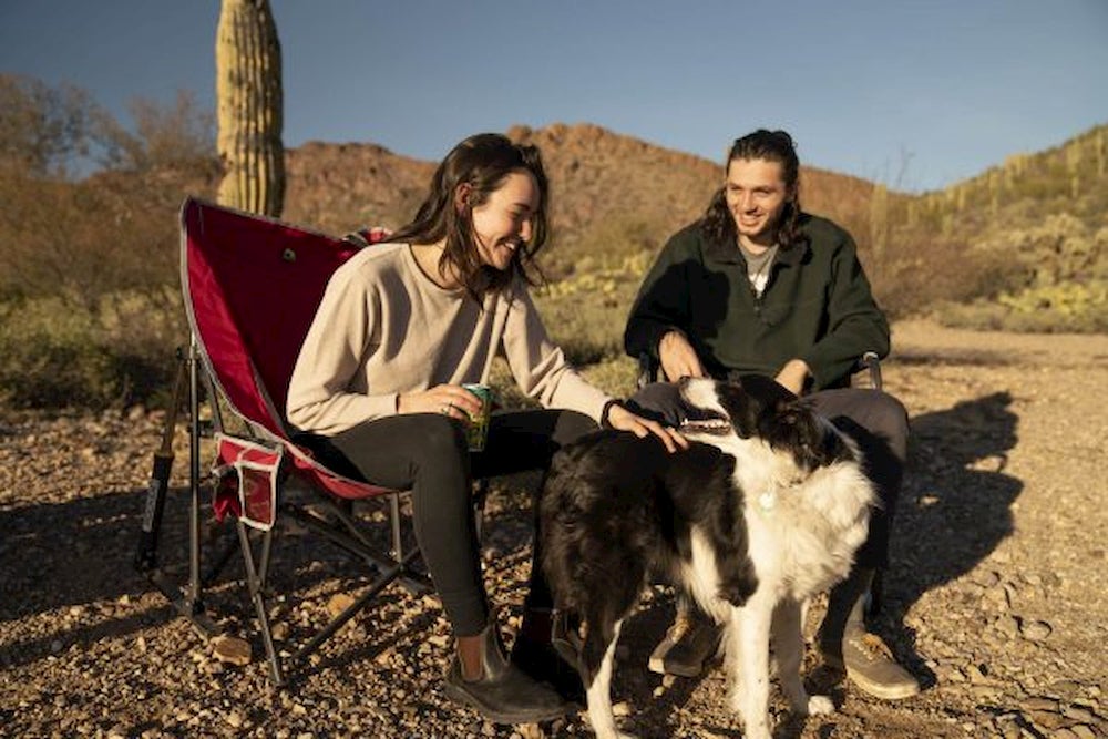 Couple sitting in camp chairs in the desert petting a dog.