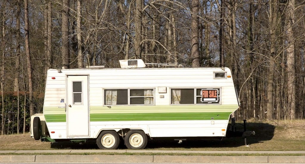 a towable camper trailer on the side of a road with a for sale sign on it