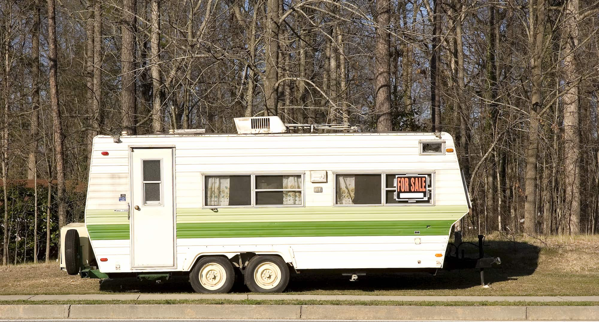 a towable camper trailer on the side of a road with a for sale sign on it