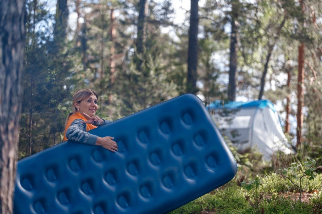 a woman smiling holding a camping air mattress at a campground
