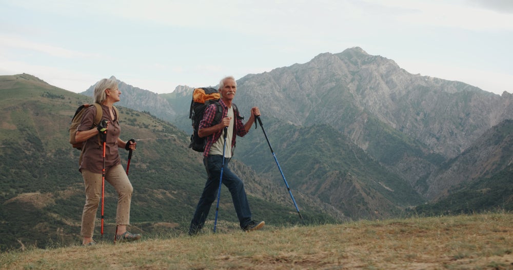 a retired couple hiking on a trail with mountains in the background