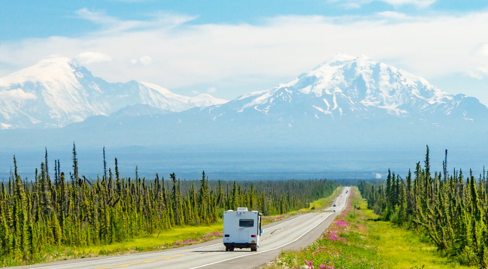 RV driving toward snow-capped mountains on a scenic road