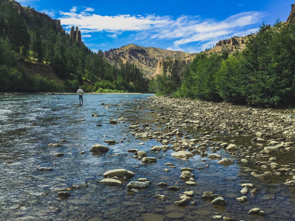 a man stands in a wide shallow river with a fishing rod 