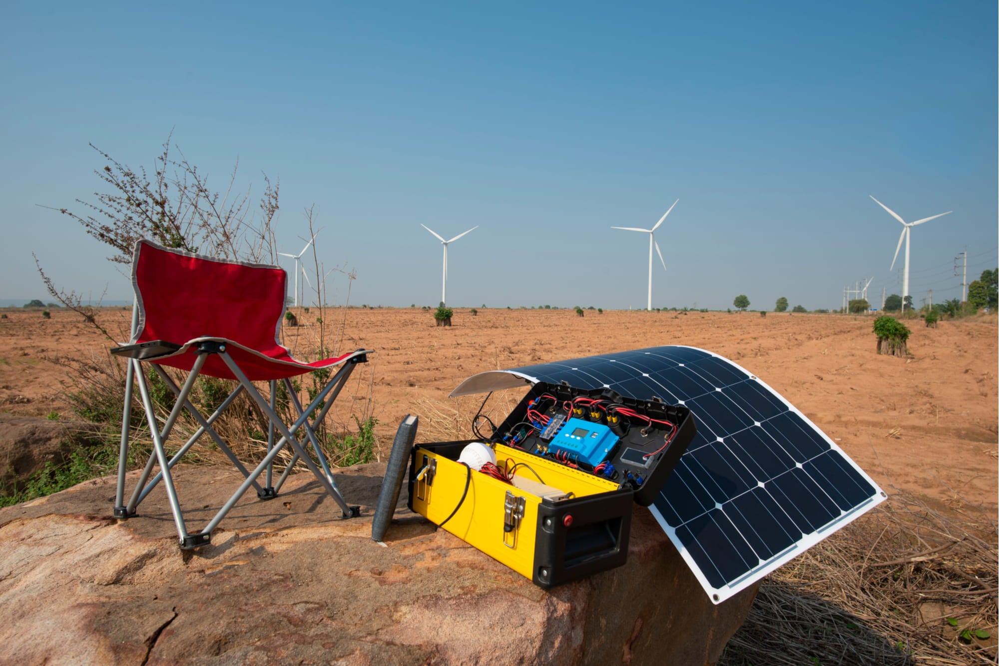 a chair next to a solar generator in a desert near wind turbines