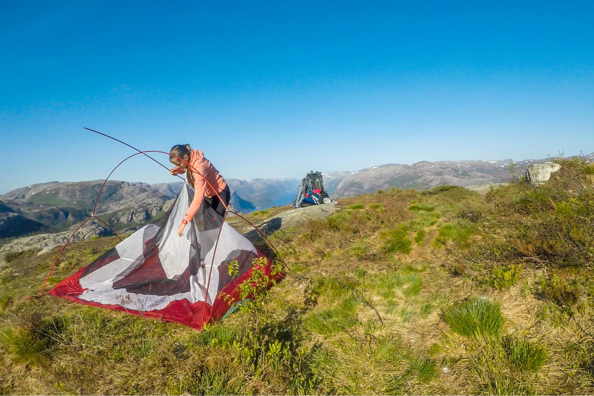 a woman struggling to set up a tent on a bald near a cliff