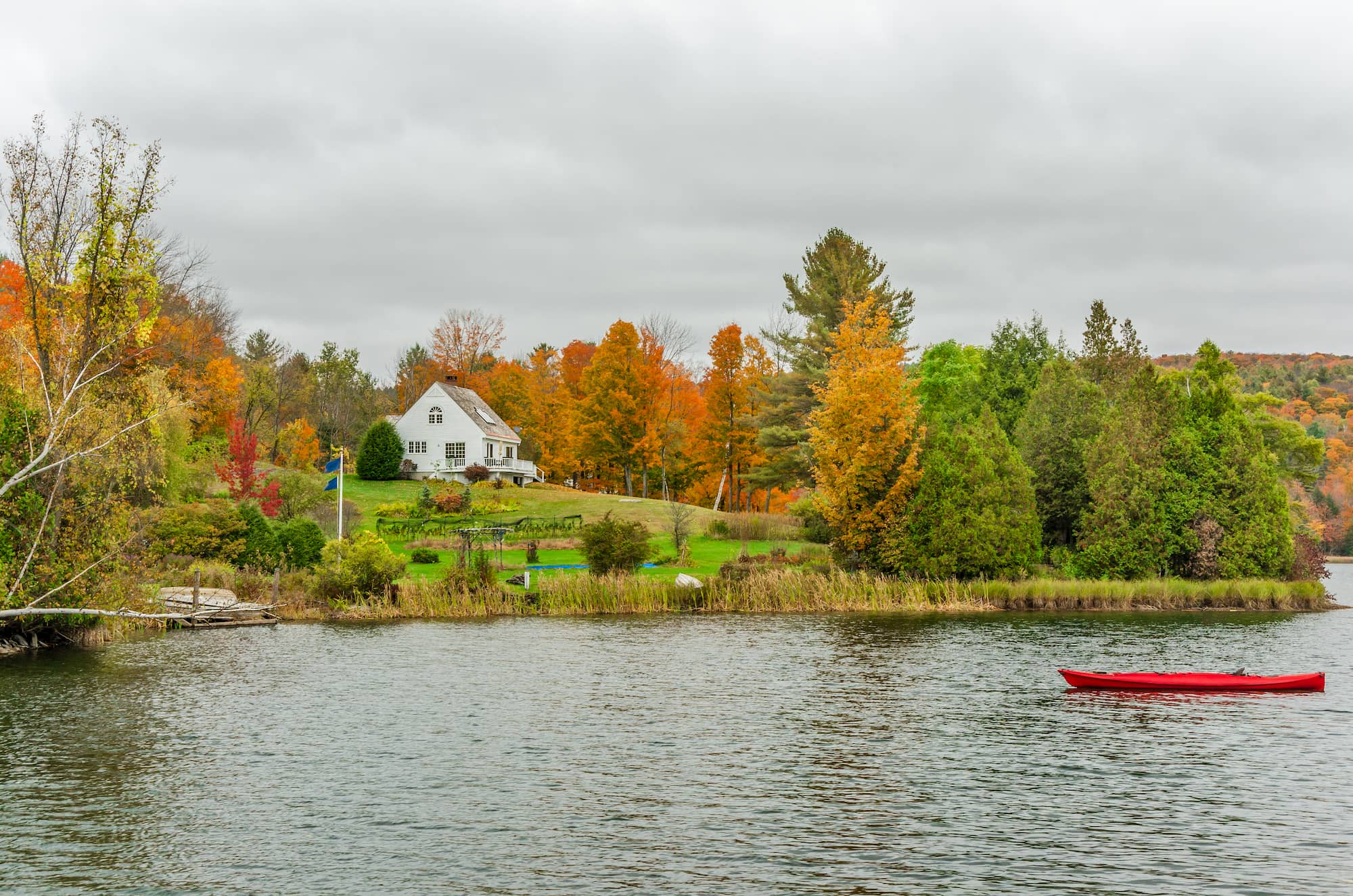 Panoramic view of fall trees, a lake, and a red canoe on the water.