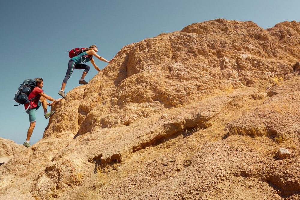 two hikers climbing orange rocks in the desert