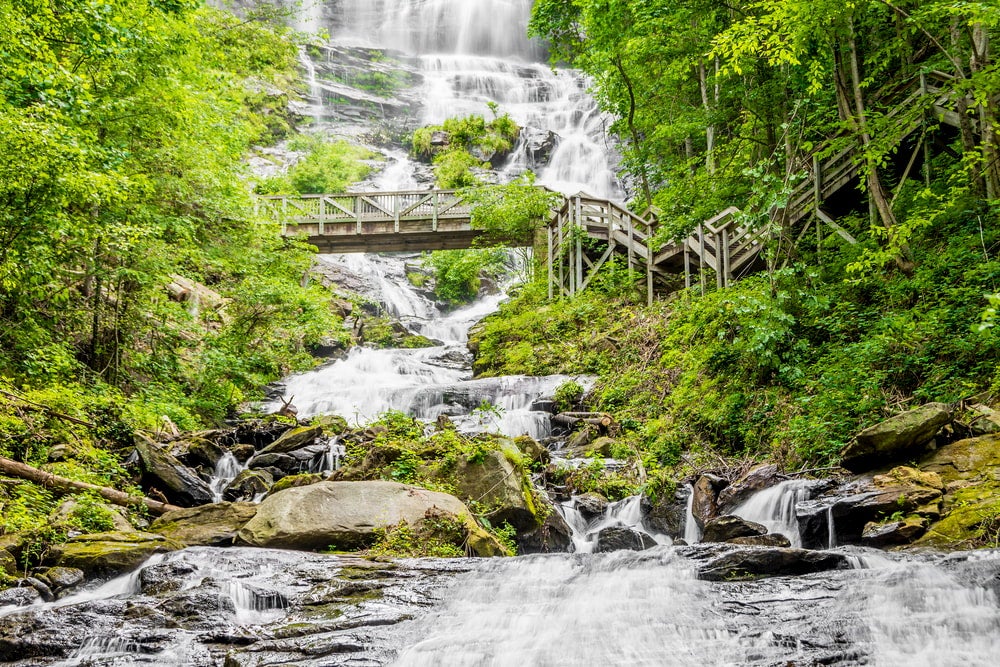 trees surround wooden bridge that crosses rocky waterfalls in amicalola falls state park