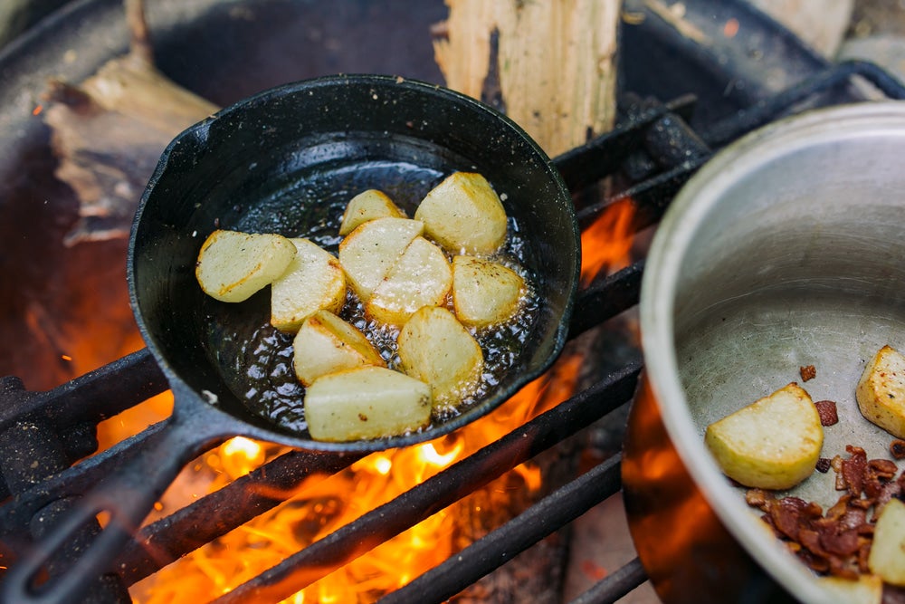 a pan cooking potatoes over an open fire at a campsite