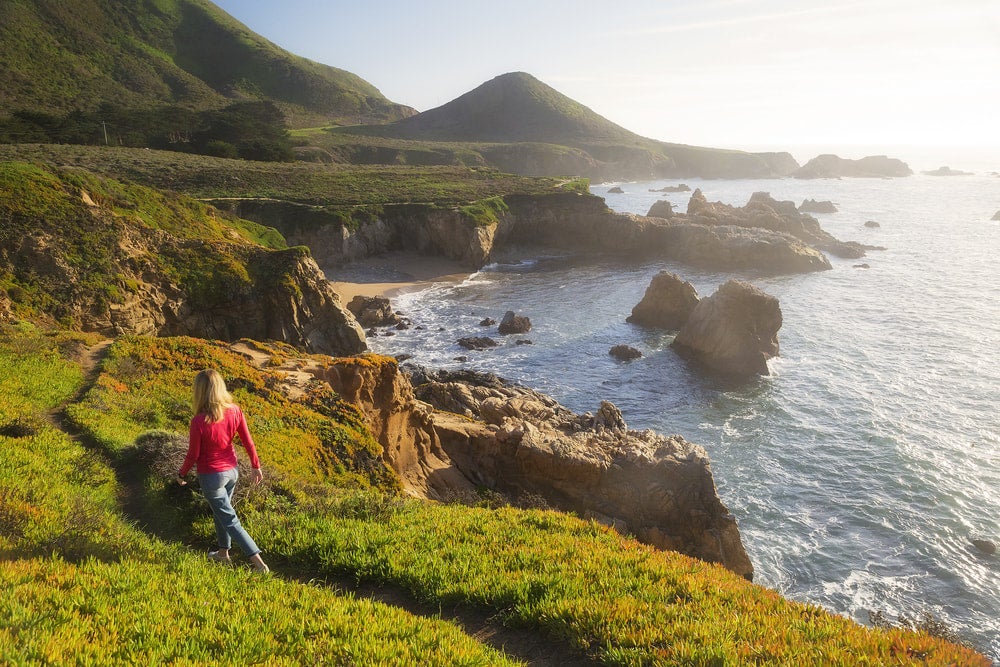 a woman hiking along a path on the coast of big sur