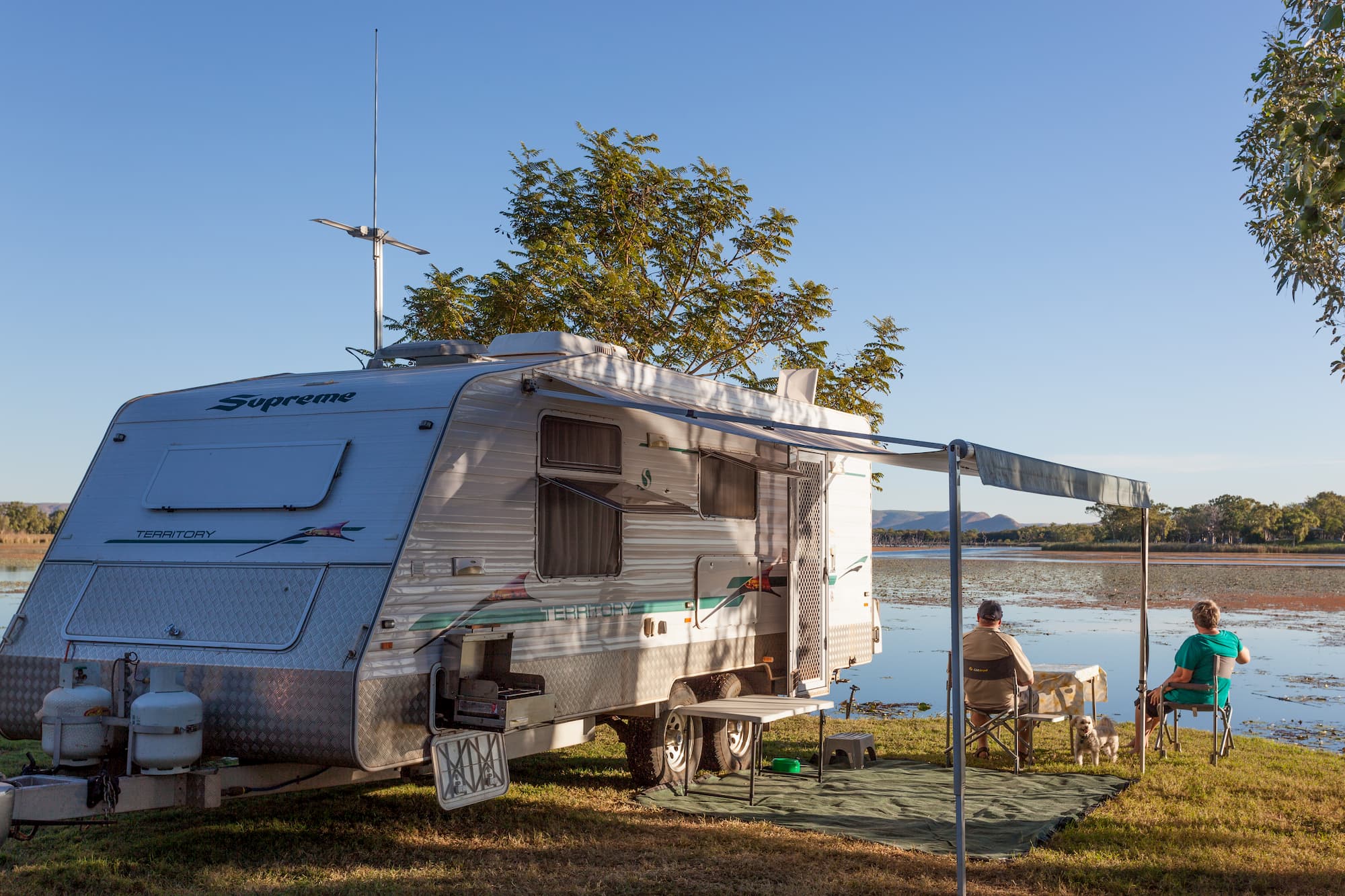 an elderly couple relaxing next to their RV camper near a lake