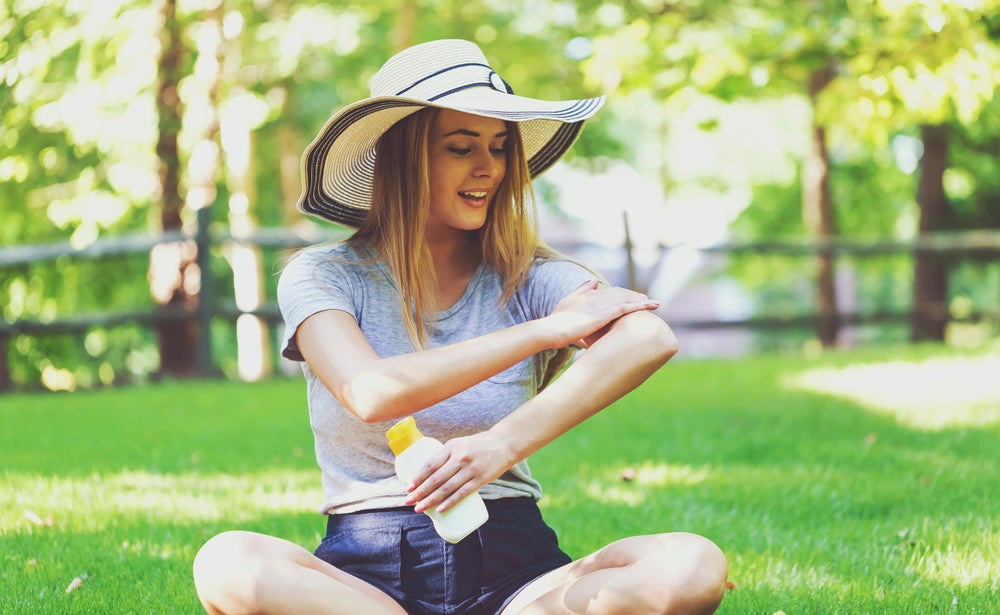 Woman in a park applying sunscreen to her arm