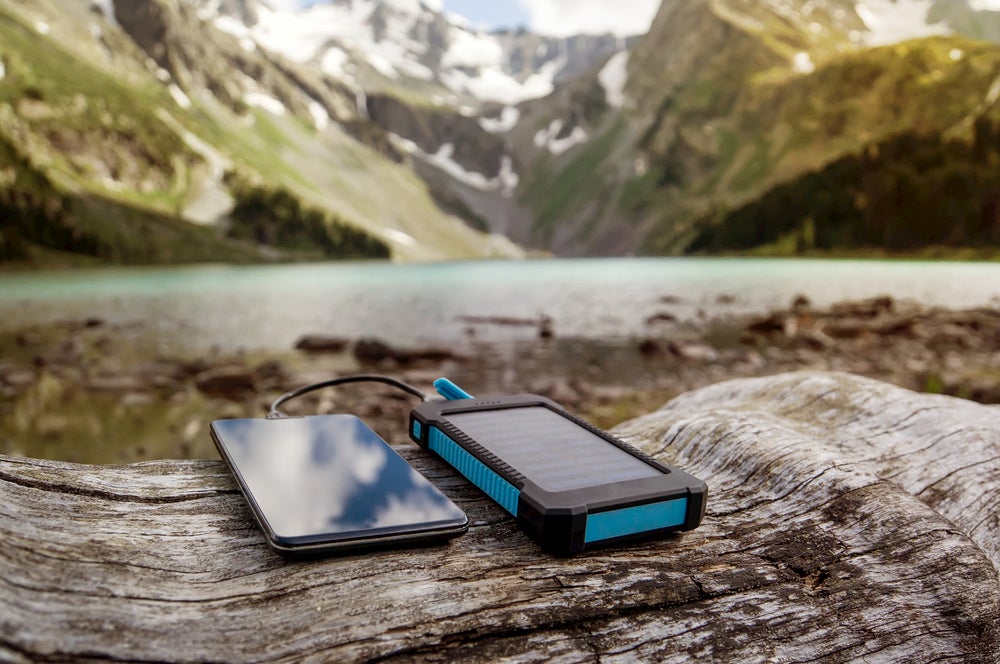 Phone and charger resting on a log with mountain scenery in background